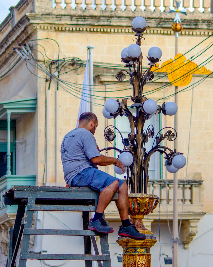 Junger Mann bringt in Naxxar eine Straßendekoration für das Ortsfest an